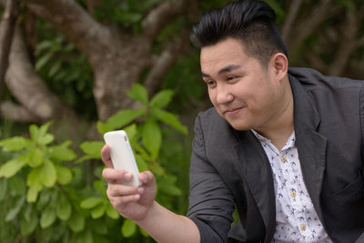 Smiling man using mobile phone against plants