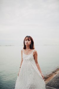 Portrait of young woman standing by sea against sky