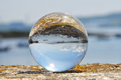 Close-up of crystal ball with reflection of rocks at lakeshore