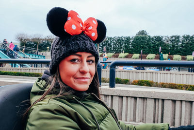 Portrait of smiling young woman wearing knit hat sitting in ride against sky