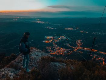 High angle view of young woman standing on mountain against cloudy sky during sunset