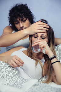 Young woman with man drinking water on bed at home