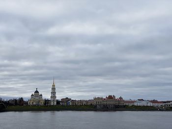 View of buildings by river against cloudy sky