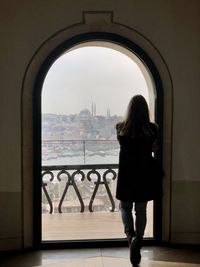 Rear view of woman looking through window in city