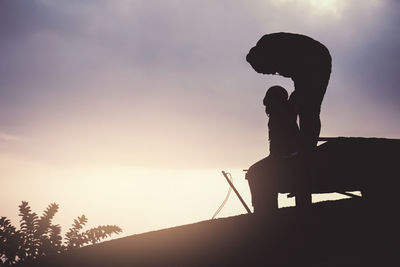 Silhouette man sitting on seat against sky during sunset