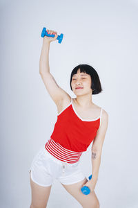 Young woman exercising with dumbbell against gray background