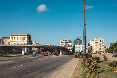 Road by buildings against blue sky in city