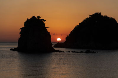 Silhouette rock on sea against sky during sunset