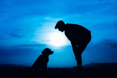 Silhouette of a young man with his dog in blue night light