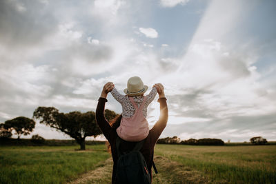 Mother carrying daughter on shoulders against cloudy sky