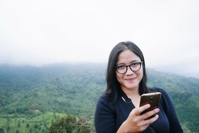 Young woman using mobile phone on mountain against sky