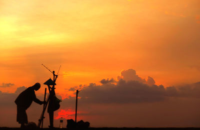 Fisherman standing against cloudy sky during sunset