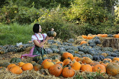 Young woman sitting by pumpkins on field