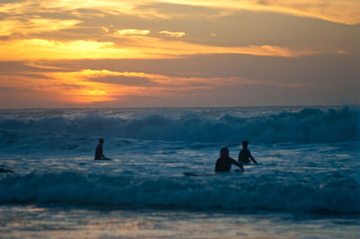 Silhouette people standing in sea against sky during sunset