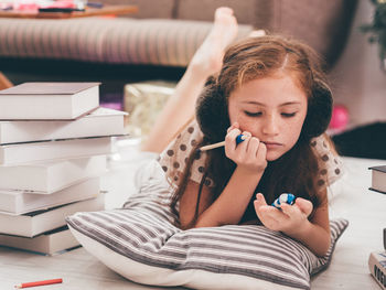 Thoughtful teenage girl lying on carpet while holding pencil and toy 