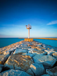 Lighthouse by sea against blue sky