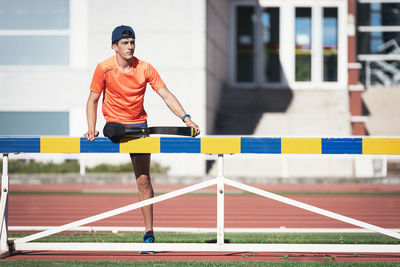 Young athlete with prosthetic leg standing by railing on running track