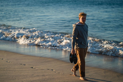 Full length of man with shoes walking at beach