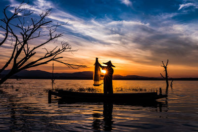 Silhouette man on boat fishing lake sea against sky during sunset