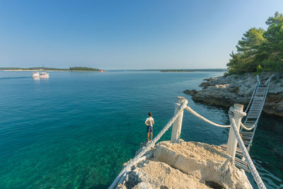 People on rock by sea against blue sky