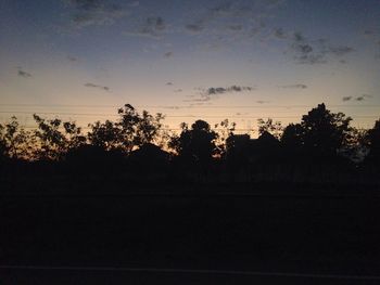 Silhouette trees on field against sky at sunset