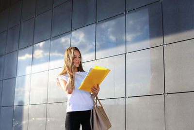 Young businesswoman talking on mobile phone while standing by wall