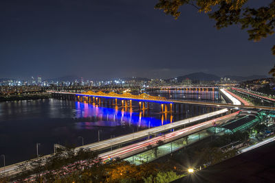 Illuminated bridge over river by city against sky at night