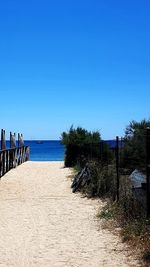 Wooden posts on beach against clear blue sky