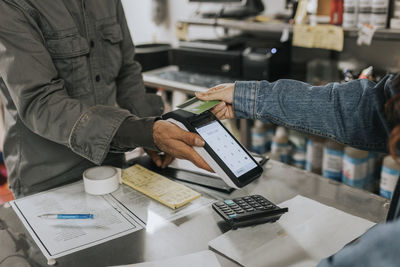 Male tailor holding credit card reader while female client making contactless payment in workshop