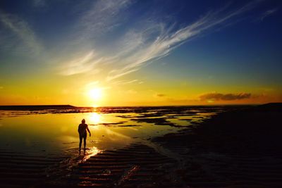 Silhouette woman walking at beach against sky during sunset