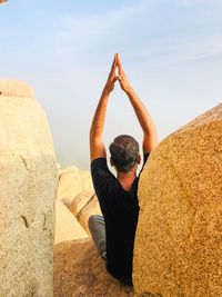 Rear view of man sitting on rock against sky