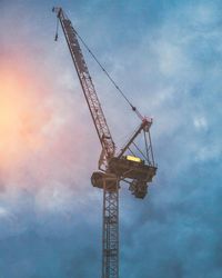 Low angle view of crane against cloudy sky during sunset
