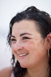 Smiling curvy female adjusting wet wavy hair and looking away on blurred background