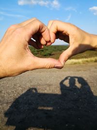 Close-up of hands forming heart shape against sky