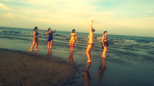 People standing on beach against sky during sunset