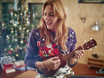 Blond woman playing ukulele in front of christmas tree