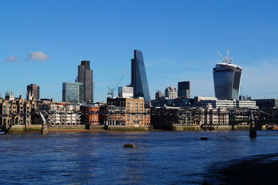 River by city buildings against blue sky