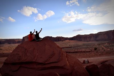 People sitting on rock formations in desert against sky