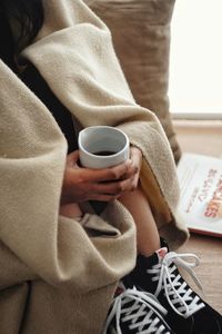 Midsection of woman holding coffee while sitting on sofa