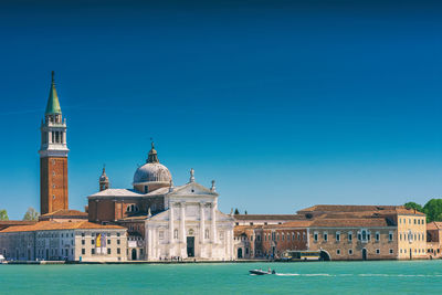 Buildings by canal against clear sky during sunny day