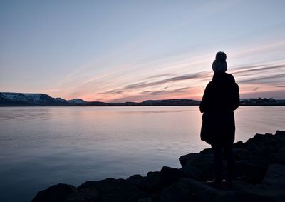 Silhouette man standing on rock against sky during sunset