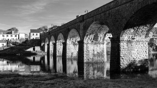 Arch bridge over canal by old building against sky