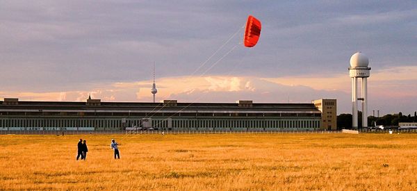 People with red kite on field against sky during sunset