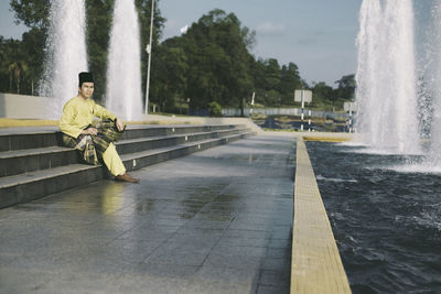 Full length of man in traditional clothing sitting on steps by fountain