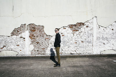 Side view of young man standing against damaged wall