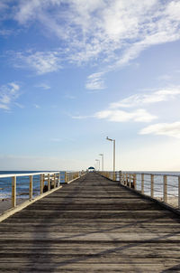 Sunlight falling on empty wooden pier over sea against blue sky