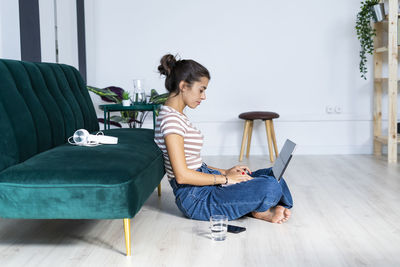 Confident female architect using laptop while sitting cross-legged on floor against sofa at office