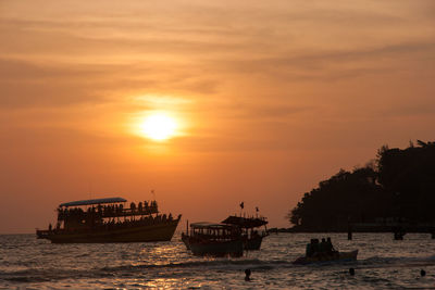 Silhouette boat sailing on sea against orange sky