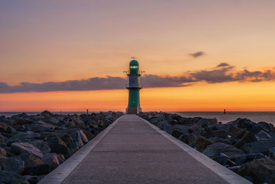 Lighthouse by sea against sky during sunset