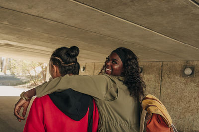 Portrait of smiling woman with arm around male friend walking together in underpass